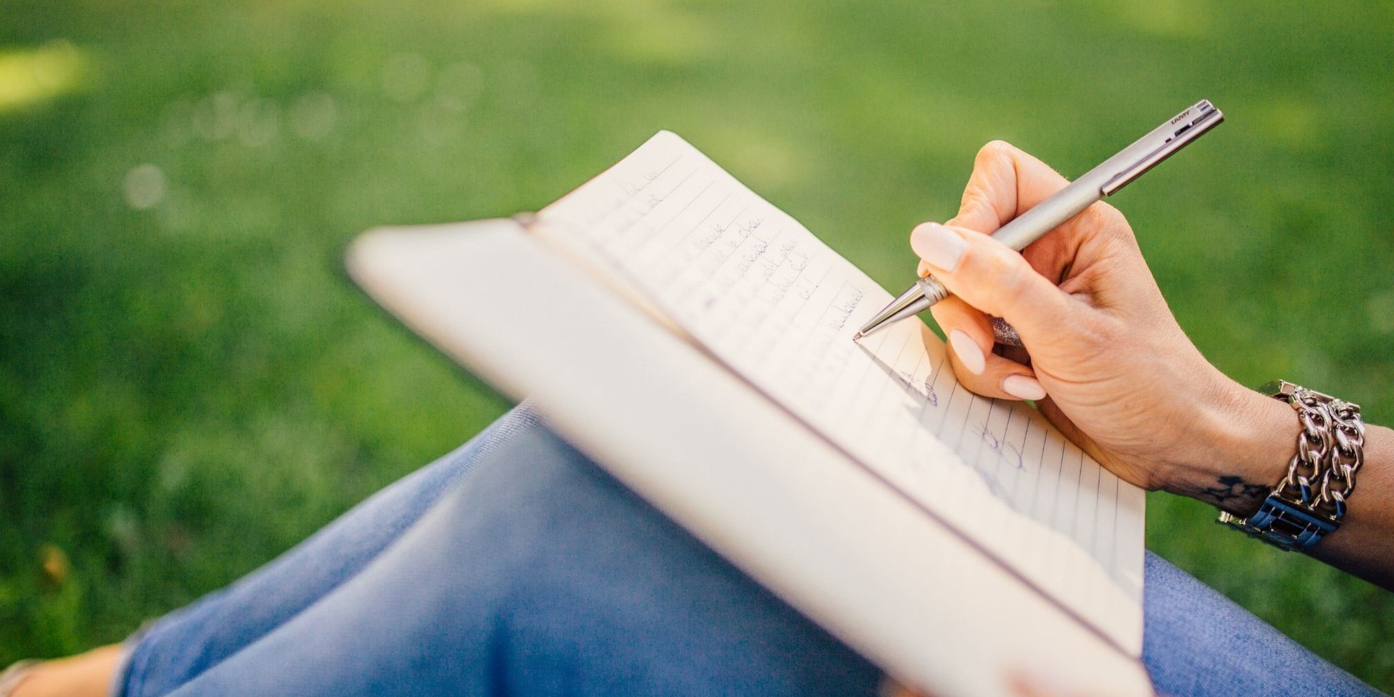 Benefits of Journaling Person writing in a notebook on a grass - Benefits of Journaling Blog Image