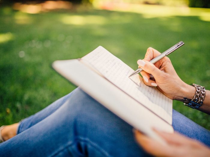Benefits of Journaling Person writing in a notebook on a grass - Benefits of Journaling Blog Image